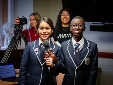 Two students smile while holding a microphone