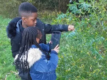 Students holding a tablet looking at leaves 