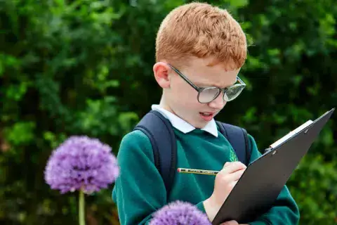A student writes on a clipboard in a garden