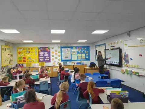 Pupils in the classroom sit at desks and listen to a teacher