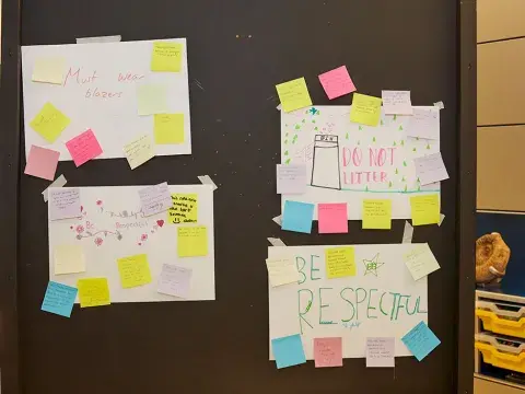 A board with four pieces of white paper with writing on them surrounded by colourful post-it notes